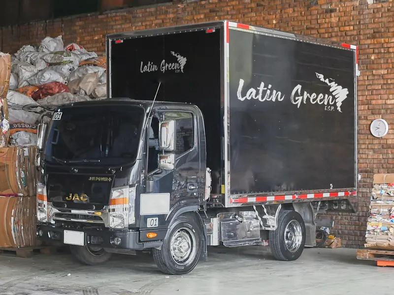 Camión furgón negro de Latín Green E.S.P., con el logo de la empresa en el costado, estacionado frente a un muro de ladrillo