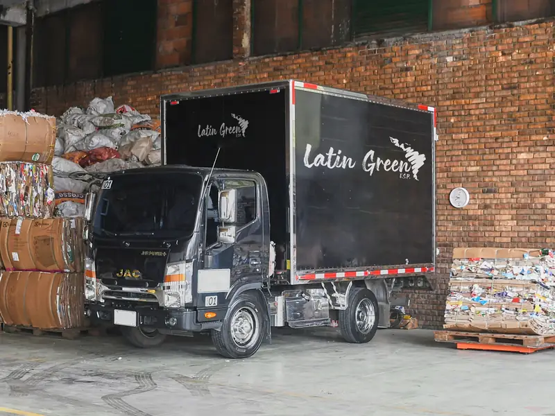 Camión furgón de Latín Green E.S.P. estacionado en la bodega, junto a pacas de cartón compactado y sacos de material reciclable